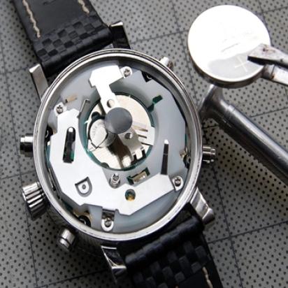 Back of a watch opened, showing the gears, and a battery being approached to it with tweezers.