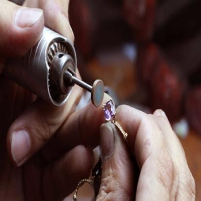 Golden ring with a purple stone being resized. Two hands show doing the work.